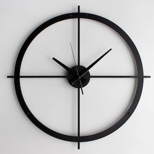 Könnte beinhalten: Eine moderne, minimalistische Wanduhr mit einem schwarzen kreisförmigen Rahmen und schwarzen Zeigern. Die Uhr hat ein Kreuzdesign innerhalb des Kreises und den Text "Black Hands" unten. Die Uhr ist an einer weißen Wand befestigt.