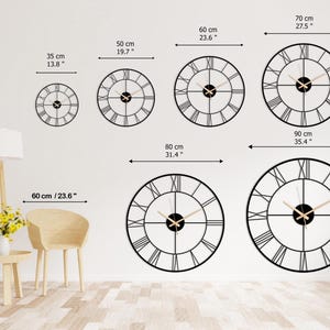May include: A collection of black metal wall clocks with Roman numeral hour markers. Sizes range from 13.8 inches to 35.4 inches in diameter. The clocks have gold-colored hands and are displayed on a white wall.