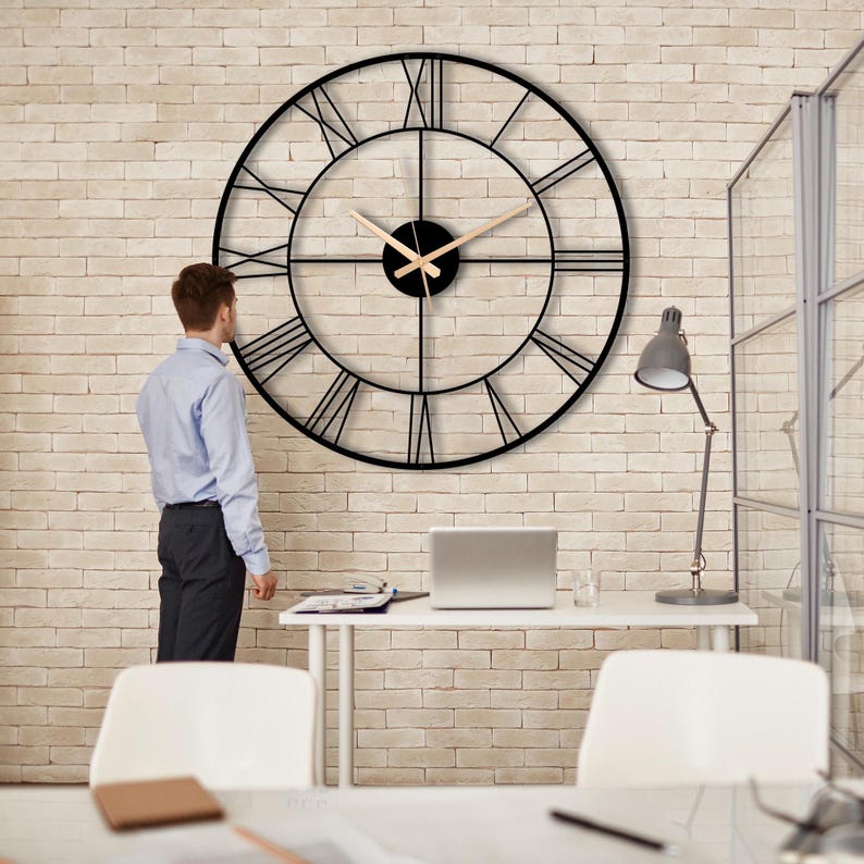 May include: A large black metal clock with Roman numeral markings on a white brick wall. The clock has a gold-colored hour and minute hand.