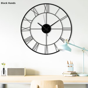 May include: A large, black metal wall clock with Roman numerals. The clock has a circular design with a minimalist aesthetic. The hands and center of the clock are also black. The clock is mounted on a white wall.