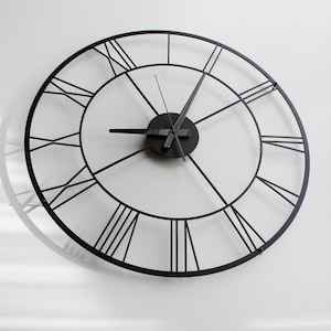 May include: A large, round, black metal wall clock with Roman numerals. The clock has a minimalist design with a circular frame and black hands. The clock's diameter is approximately 30 inches.