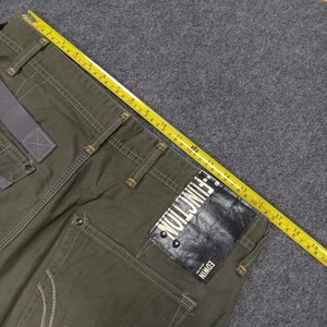 Op de afbeelding: Groene cargo broek met meerdere zakken en een zwart lederen patch met de tekst "E-FUNCTION EDWIN".