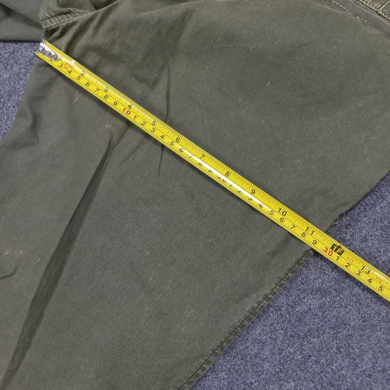 May include: A close-up of a green fabric with a seam along the edge. A yellow measuring tape is laid across the fabric, showing measurements in inches.