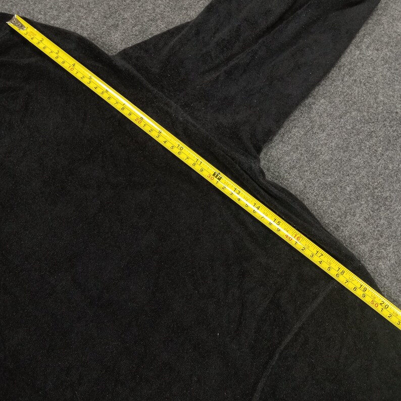Puede incluir: Una camisa negra de manga larga con una cinta m&eacute;trica amarilla colocada sobre ella. La cinta mide 50,8 cm.