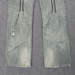 May include: Light blue denim jeans with a zipper detail down the front. The jeans have a faded wash and a distressed look, with some wear and tear visible. The jeans are a classic five-pocket style.