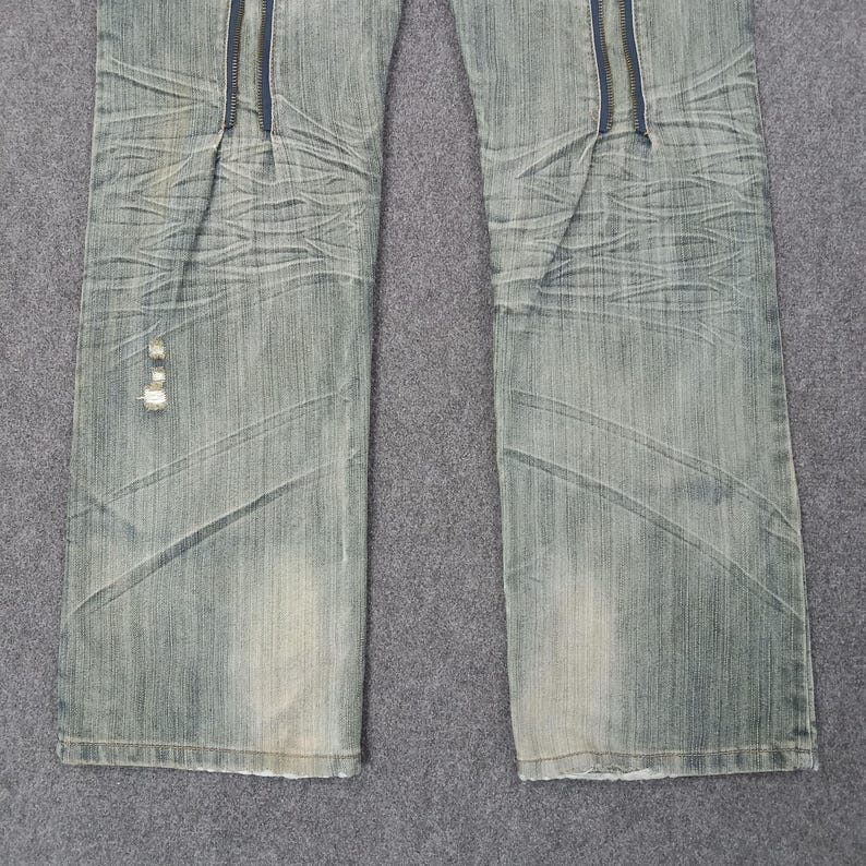 May include: Light blue denim jeans with a zipper detail down the front. The jeans have a faded wash and a distressed look, with some wear and tear visible. The jeans are a classic five-pocket style.