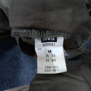 May include: A brown clothing tag with white text that reads "EDWIN. K50581 SIZE M W 78 H 96 ERM-1769 E231-2011"