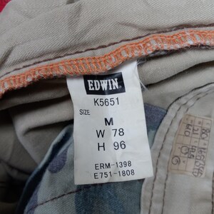 May include: A beige and orange clothing label with the text "EDWIN" and the model number "K5651". The label also includes the size "M", waist measurement "W 78", hip measurement "H 96", and the numbers "ERM-1398" and "E751-1808".