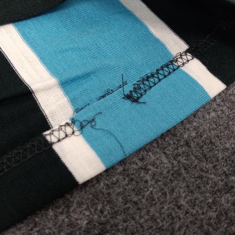 May include: Close-up of a black and white striped fabric with a blue stripe. The fabric is sewn together with a black thread.