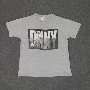 May include: Grey short-sleeved t-shirt with a black and white graphic print of the word "DKNY" with a cityscape in the background.