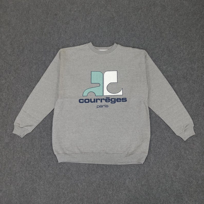 May include: A gray crew neck sweatshirt with the Courr&egrave;ges logo in teal, white, and navy blue. The logo features the brand name and "paris" in a sans-serif font. The sweatshirt is made of a soft material.