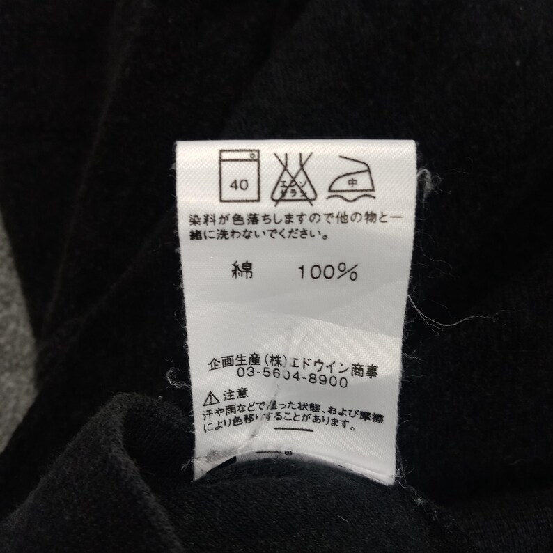 Puede incluir: Una etiqueta de cuidado blanca con texto negro y s&iacute;mbolos. La etiqueta incluye instrucciones de lavado, composici&oacute;n del tejido e informaci&oacute;n del fabricante. El texto dice: "40", "染料が色落ちしますので他の物と一緒 に洗わないでください。", "綿 100%", "企画生産(株)エドウイン商事 03-5604-8900", "▲注意 汗や雨などで塗った状態、および摩擦 により色移りすることがあります。"