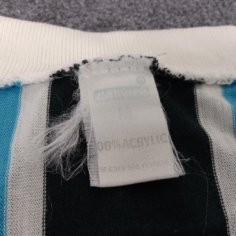 May include: A white tag with black text that reads "100% Acrylic" and "Made in China" attached to a black and white striped shirt with a blue stripe.