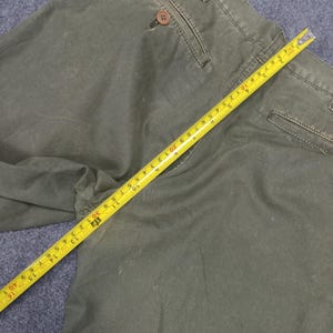 May include: A pair of olive green cargo trousers with a measuring tape laid across them. The tape measure reads 30 inches.