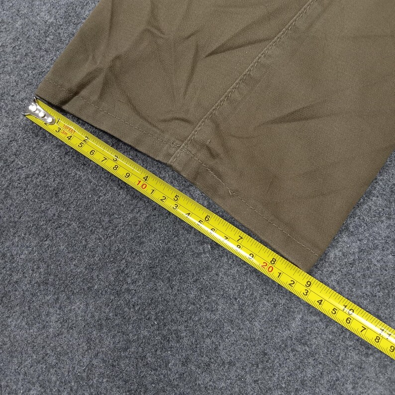 May include: Close-up of a brown fabric with a seam running down the center. A yellow measuring tape is laid across the fabric, showing measurements in inches.