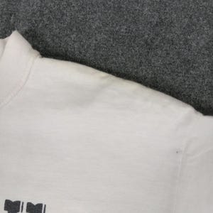 May include: White crew neck t-shirt with a printed design at the bottom. The shirt has a ribbed collar and short sleeves. The fabric appears to be a soft, lightweight material.