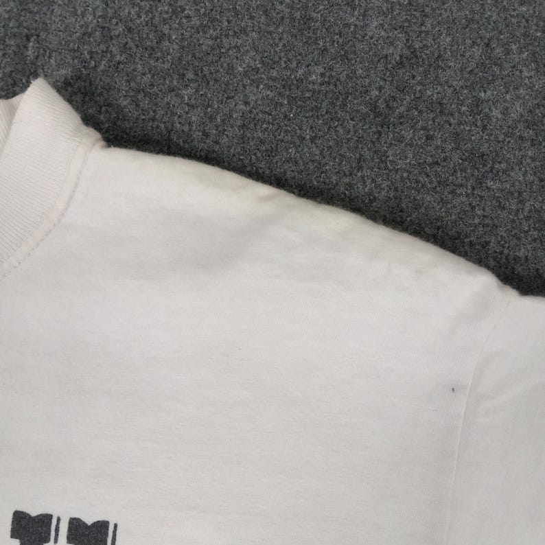 May include: White crew neck t-shirt with a printed design at the bottom. The shirt has a ribbed collar and short sleeves. The fabric appears to be a soft, lightweight material.