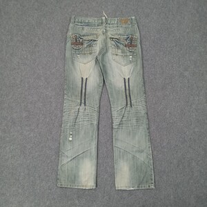 May include: Light blue denim jeans with decorative stitching and distressed details. Features unique pocket designs and dark blue vertical accents. The jeans have a classic five-pocket design and a straight leg fit.