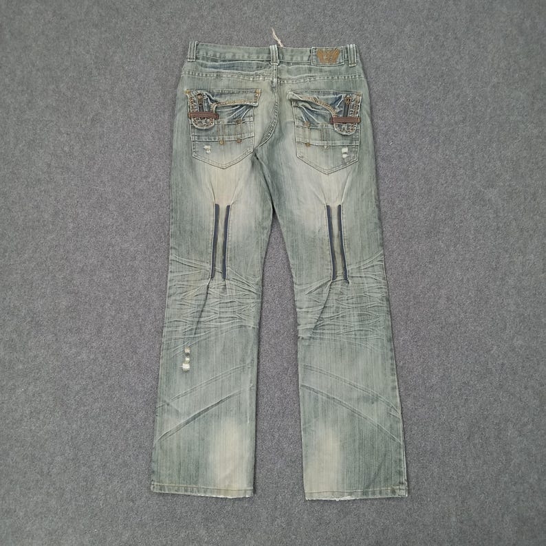 May include: Light blue denim jeans with decorative stitching and distressed details. Features unique pocket designs and dark blue vertical accents. The jeans have a classic five-pocket design and a straight leg fit.