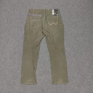 Op de afbeelding: Een olijfgroene cargo broek met een grijze tailleband en een geel label op de achterzak.