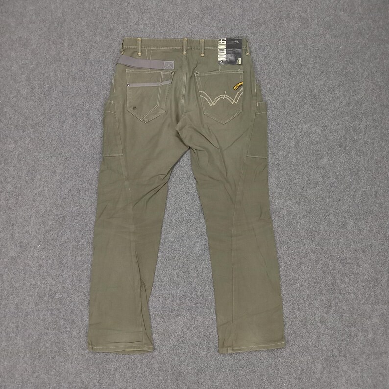 Op de afbeelding: Een olijfgroene cargo broek met een grijze tailleband en een geel label op de achterzak.