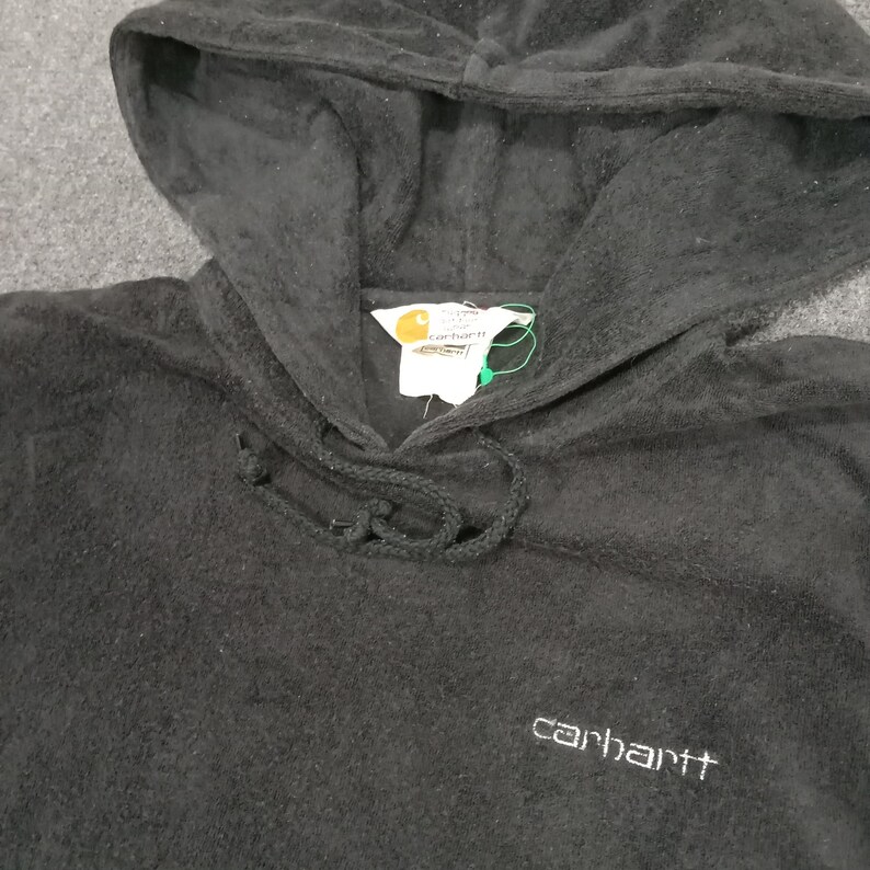 Puede incluir: Sudadera con capucha negra con un logotipo de Carhartt bordado en la parte delantera. La sudadera tiene un cord&oacute;n y un bolsillo canguro.