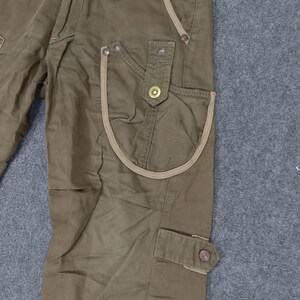 May include: Brown cargo pants with multiple pockets and a tan trim detail. The pants have a relaxed fit and a straight leg.