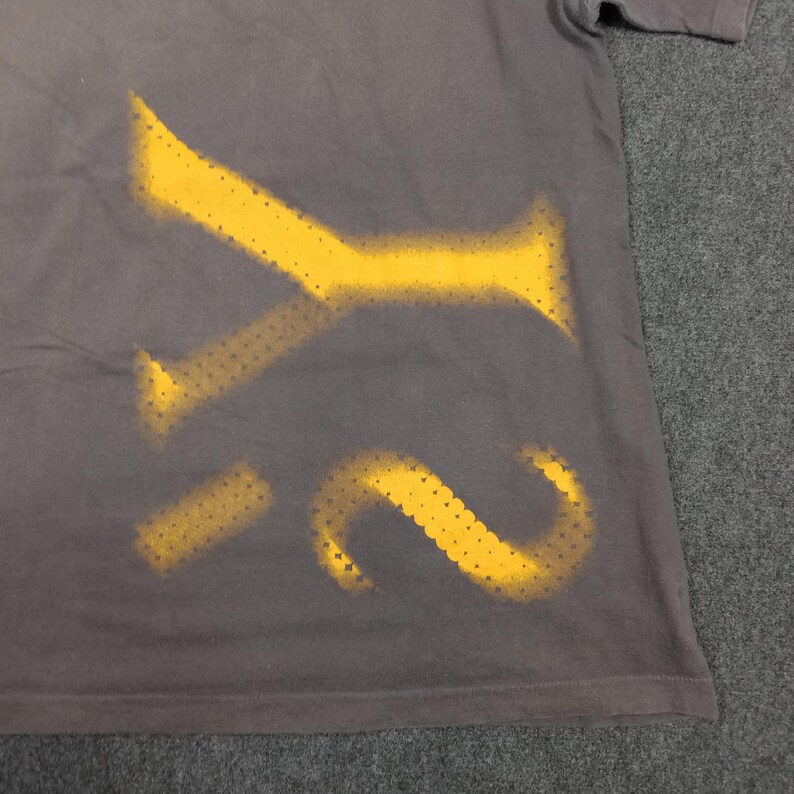 Puede incluir: Camiseta gris con un dise&ntilde;o amarillo estilo plantilla de las letras "Y2". La pintura amarilla tiene un patr&oacute;n de puntos. La camiseta est&aacute; hecha de un material suave, adecuado para ropa casual. El dise&ntilde;o est&aacute; en el lado inferior izquierdo.