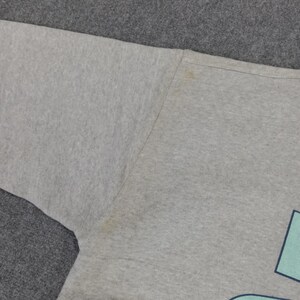 May include: A light gray sweatshirt with a faded design. The sweatshirt has a crew neck and long sleeves. There are some stains on the fabric. The design is partially visible, with a light blue shape.