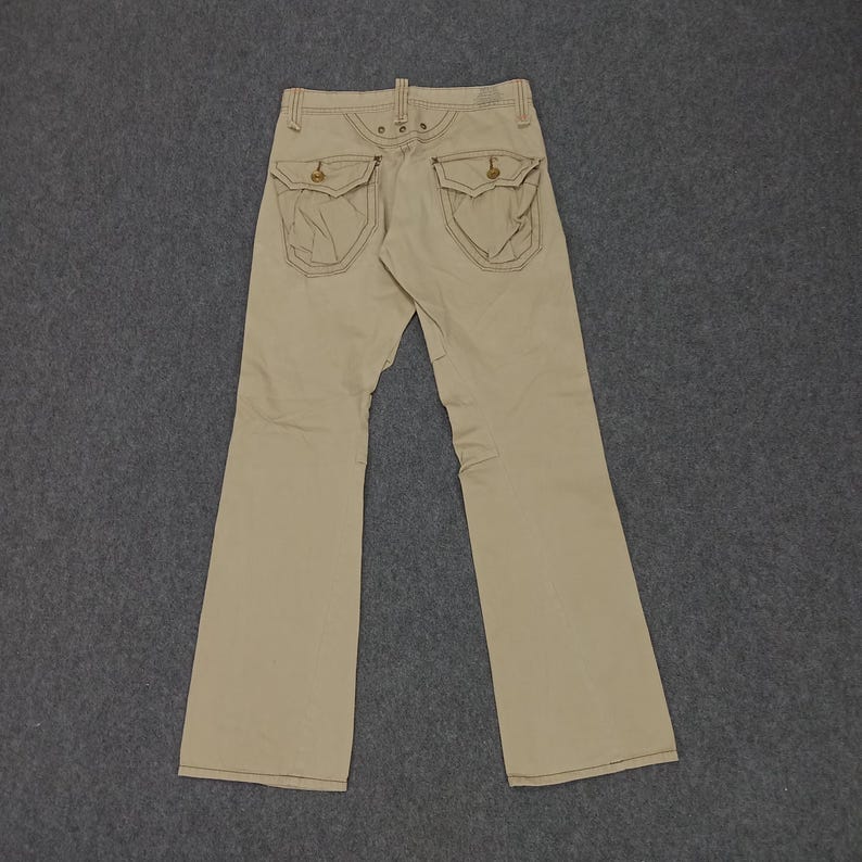 May include: A pair of beige, straight-leg pants with two large pockets on the back. The pockets have a decorative stitching detail.