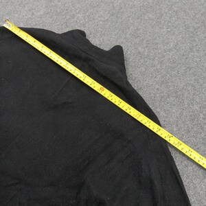 May include: A solid black long-sleeved shirt made of a soft fabric. A yellow measuring tape is placed diagonally across the garment, showing a length measurement that extends past 22 inches from the top corner to the lower edge of the fabric.