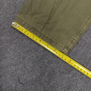 May include: Close-up of the bottom edge of a pair of olive green cargo trousers. A yellow measuring tape is laid across the fabric.