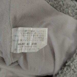 Op de afbeelding: Een wit label met zwarte tekst die luidt "(株)ワイズフォーリピング 03-6408-0131 MADE IN JAPAN ・裏返してネットに入れて洗って下さい。 ・中独洗いをして下さい。 充分に形を整えてから干して下さい。 ・アイロン掛けはお避け下さい。 タンブラー乾燥はお避け下さい."