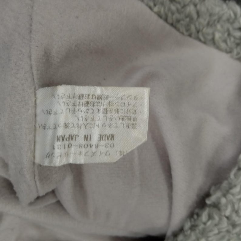 Op de afbeelding: Een wit label met zwarte tekst die luidt "(株)ワイズフォーリピング 03-6408-0131 MADE IN JAPAN ・裏返してネットに入れて洗って下さい。 ・中独洗いをして下さい。 充分に形を整えてから干して下さい。 ・アイロン掛けはお避け下さい。 タンブラー乾燥はお避け下さい."
