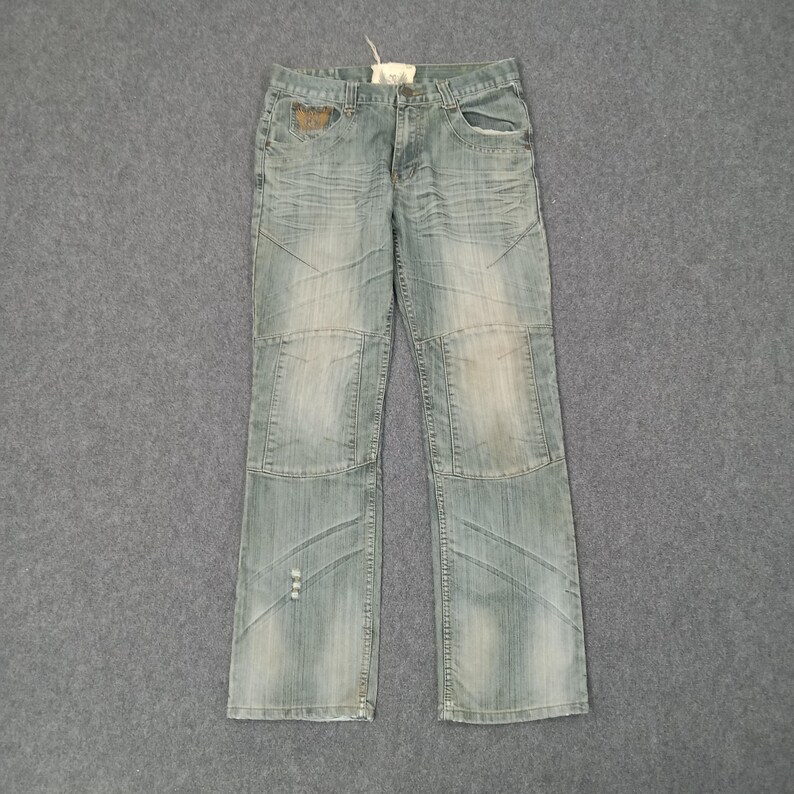 May include: Light blue denim jeans with a faded wash and distressed details. The jeans feature a classic five-pocket design, with reinforced knee panels and decorative stitching. A small tag is attached to the waistband.