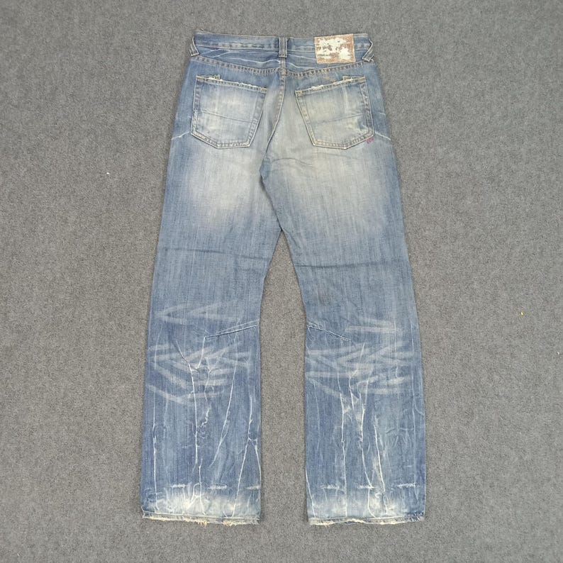 Op de afbeelding: Lichtblauwe denim jeans met een distressed look, met vervaagde plekken en witte distressed lijnen. De jeans heeft twee achterzakken en een leren patch op de tailleband. De onderste zomen zijn gerafeld.