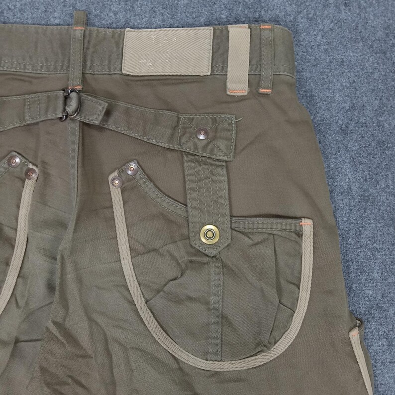 May include: Olive green cargo pants with a brown fabric trim around the pockets. The pants have a belt loop and a button closure.