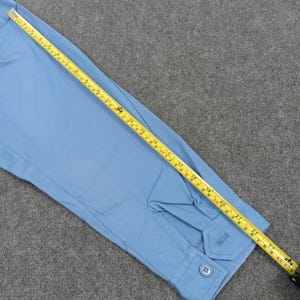 Puede incluir: Camisa azul claro de manga larga con pu&ntilde;o abotonado y tapeta abotonada. Una cinta m&eacute;trica amarilla se coloca sobre la camisa, mostrando medidas en cm.