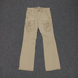 May include: Beige cargo pants with multiple pockets and a stitched design. The pants have a straight leg and a relaxed fit.