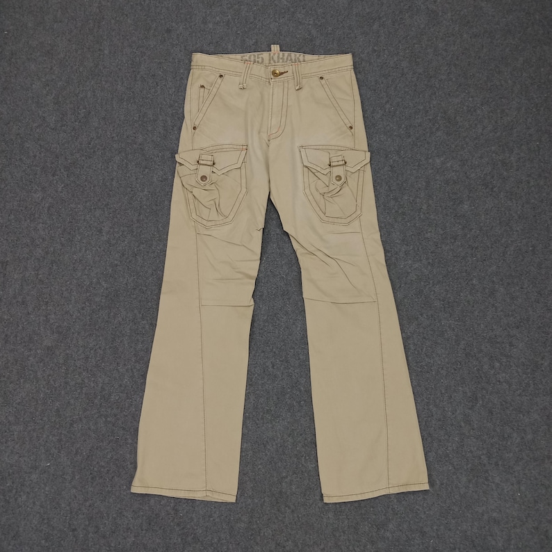 May include: Beige cargo pants with multiple pockets and a stitched design. The pants have a straight leg and a relaxed fit.