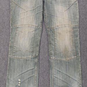 May include: Light blue denim jeans with a faded wash and patchwork design. The jeans feature reinforced knee panels and decorative stitching. The denim has a worn appearance.