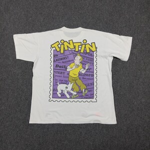 May include: White t-shirt featuring a graphic of Tintin and Snowy in a purple postage stamp design. The design includes the word "TINTIN" in yellow and the text "Daily" and "Mystery". The shirt is a classic, vintage style.