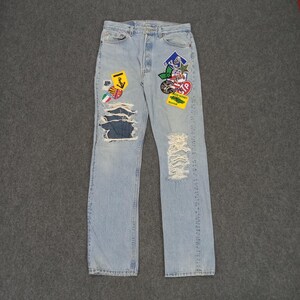 May include: Light blue denim jeans with multiple patches and distressed details. The patches feature various designs, including a yellow anchor, a red stop sign, and a green and white car.