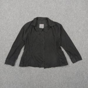 May include: A solid black long-sleeved jacket featuring a pointed collar, a front button closure, and two side pockets. The garment has a structured fit with a straight hemline and a small white brand label attached to the inside of the collar.