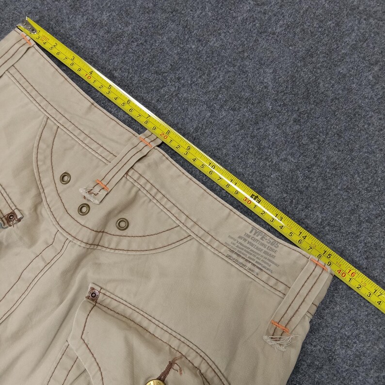 May include: Beige cargo pants with brown stitching and a label that reads "TYPE-505 THE CUTTING EDGE"