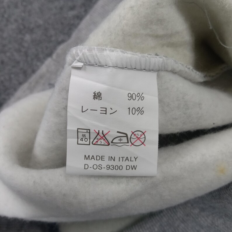 May include: Close-up of a clothing tag with Japanese characters and the words "MADE IN ITALY". The tag indicates the fabric composition: 90% cotton and 10% rayon. Washing instructions are also displayed.