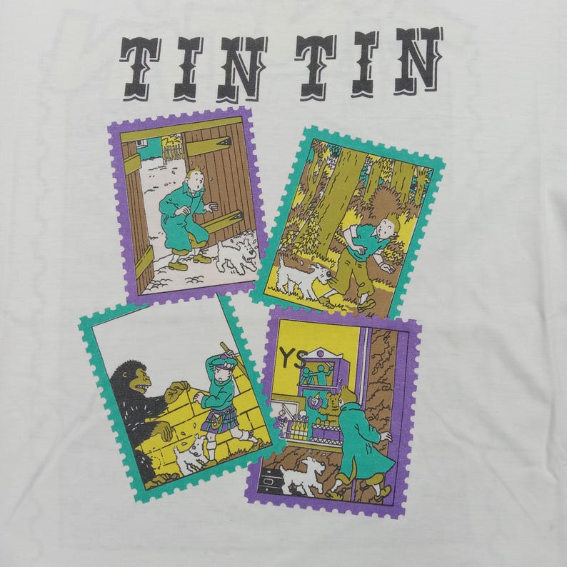 May include: White t-shirt featuring the word "TINTIN" in gray block letters above four colorful stamp-like illustrations. Each stamp depicts scenes with characters and dogs, framed in purple and green.