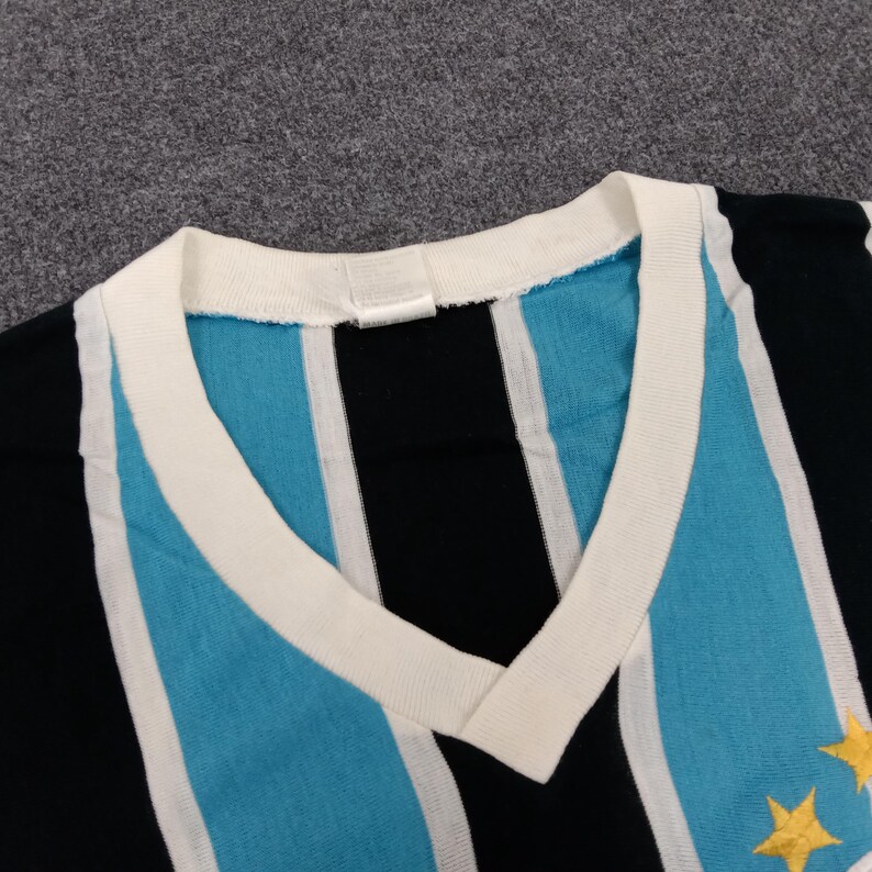 May include: A striped v-neck shirt with blue, white, and black stripes. The shirt has a white collar and two gold stars on the right side.