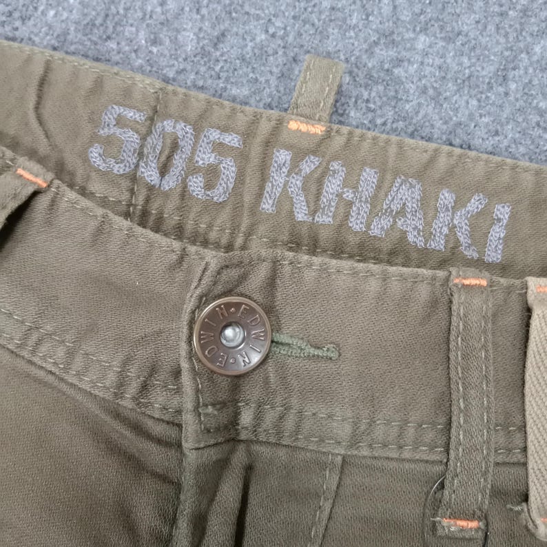 May include: Close-up of a pair of khaki pants with a button and a label that reads "505 KHAKI".