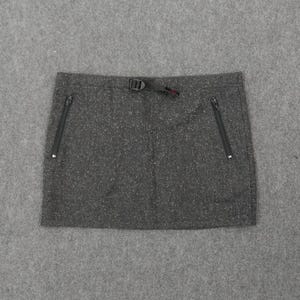 Pode incluir: Minissaia cinza com dois bolsos com z&iacute;per e fecho de fivela preto. A saia tem uma textura salpicada e um design simples e funcional, adequado para atividades ao ar livre.